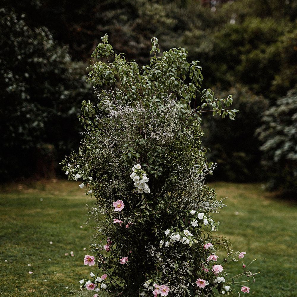 Tall flower column for altar decor with lots of greenery and white bell flowers and pink cosmos 