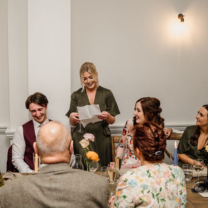 Bridesmaid in green wrap dress gives a speech while everyone listens 
