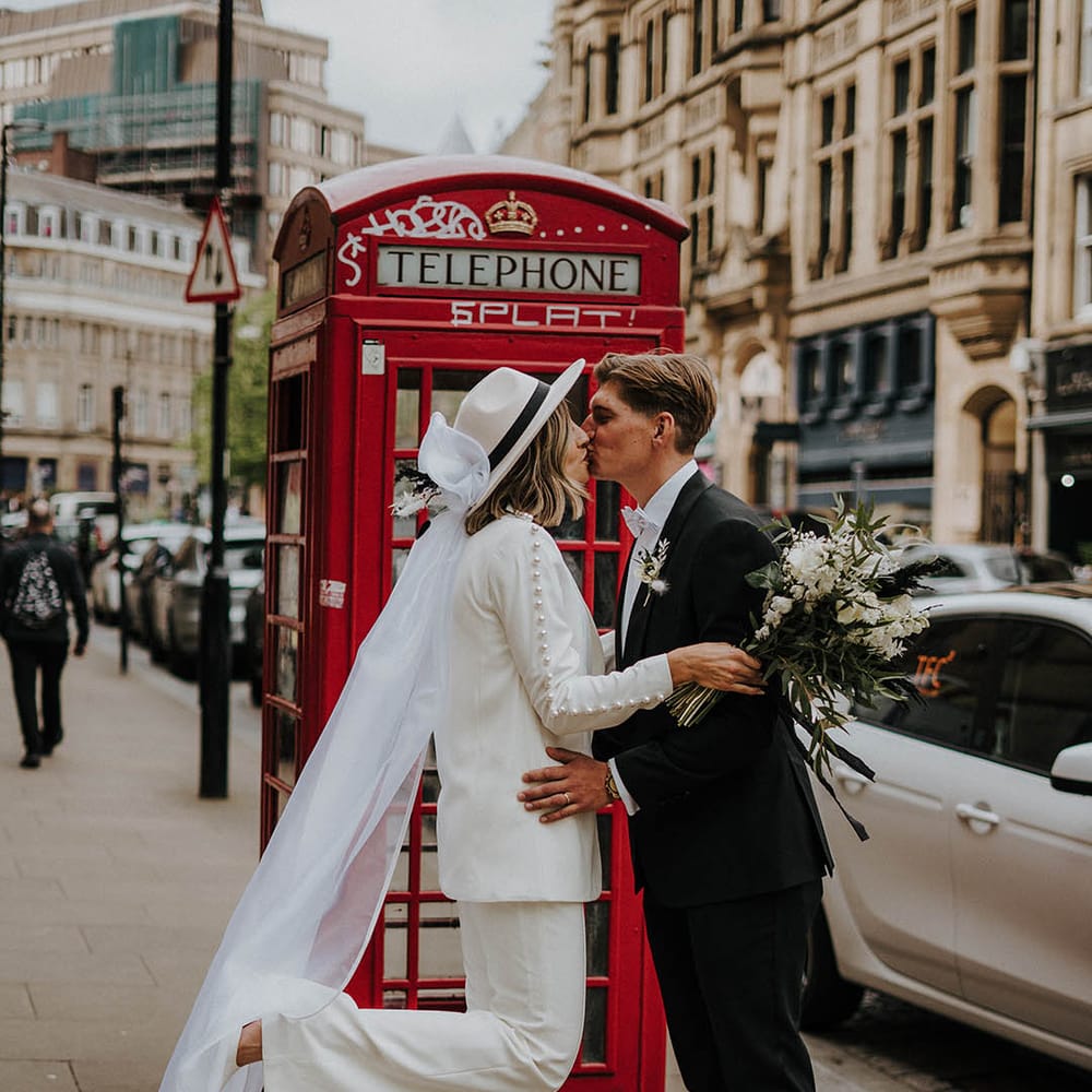 Bride and groom kiss in front of red telephone box 