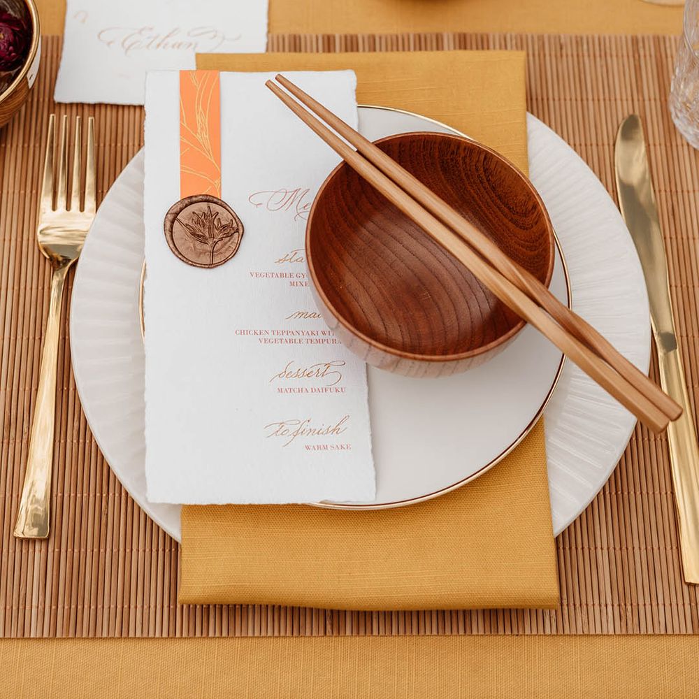Place setting with yellow table rubber, bamboo place mat, gold cutlery, brown rice bowls and wooden chopsticks for Japanese wedding 
