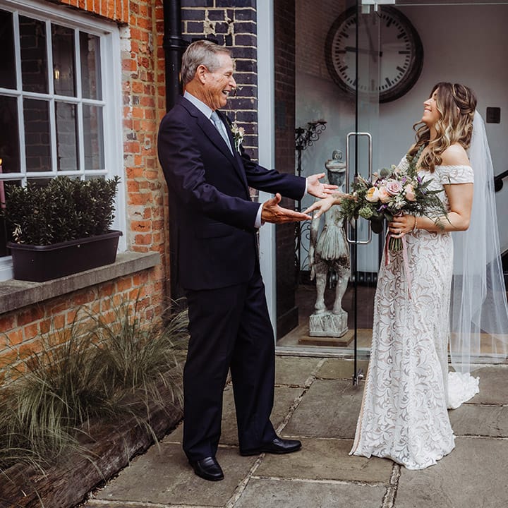 Father of the bride in a blue suit gets a first look at the bride in her off the shoulder lace wedding dress 