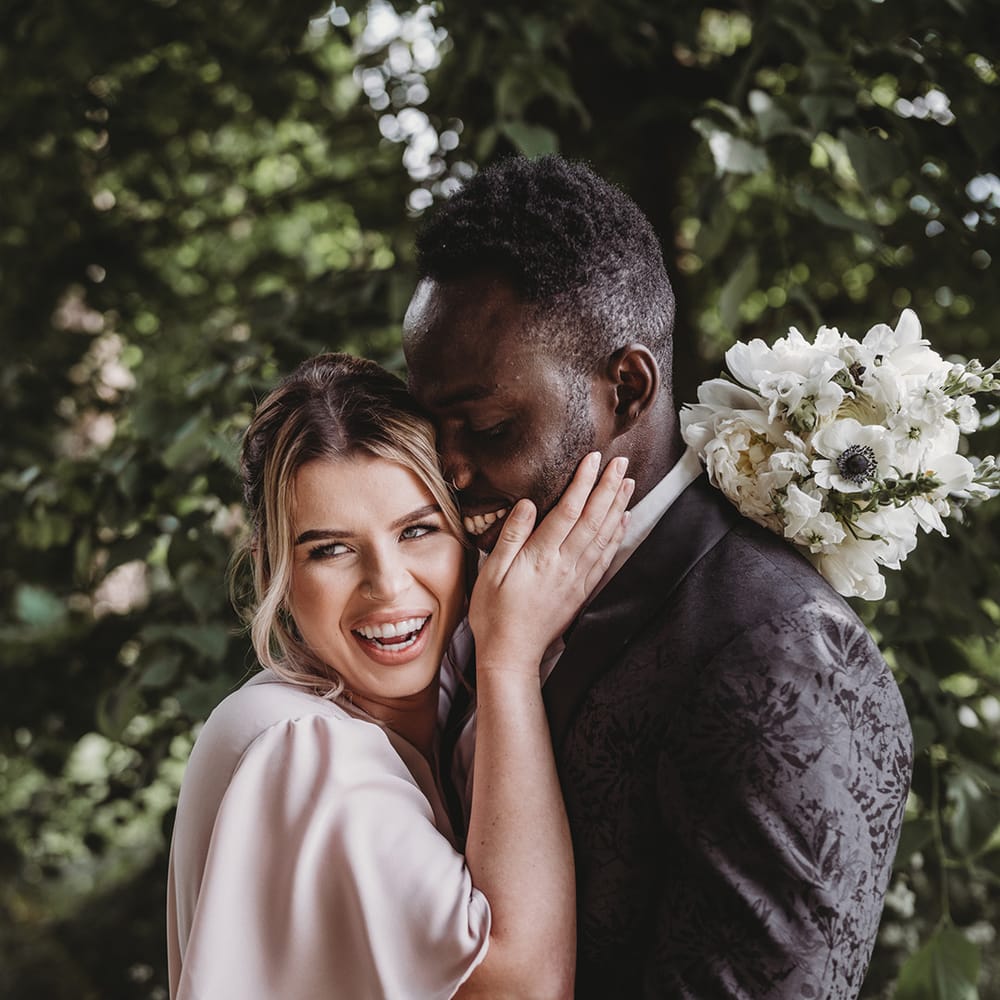 Bridesmaid in a pale pink dress hugs the groomsman in a black patterned suit jacket 
