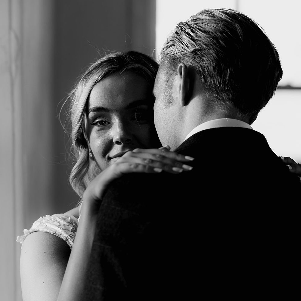 Bride looks at the camera over the groom's shoulder as they pose together for their wedding at the Badminton Estate