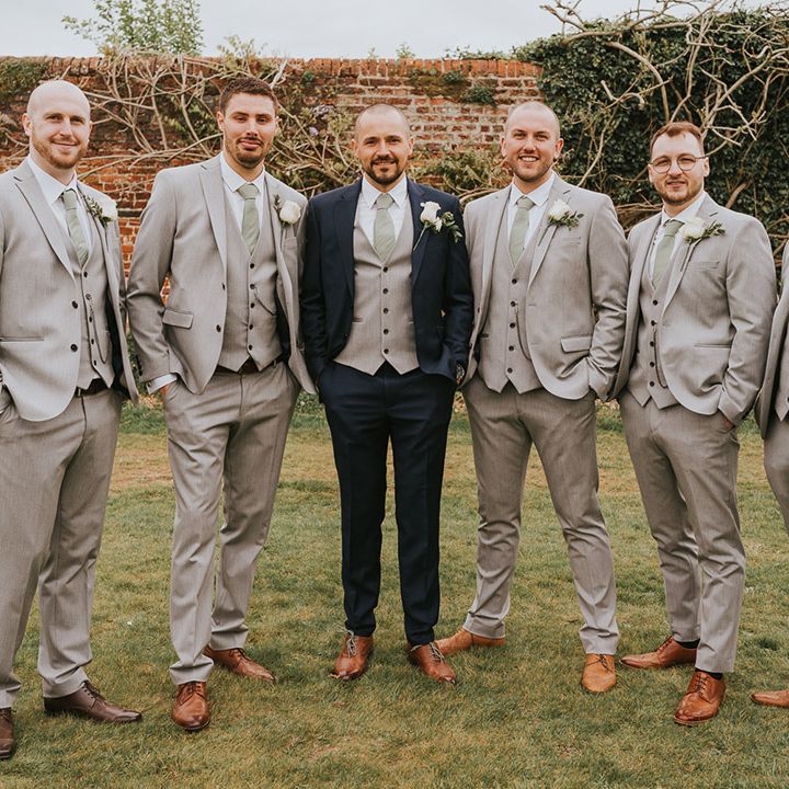 Groomsmen in pale grey suits with the groom in a dark blue suit with brown shoes and white rose buttonholes