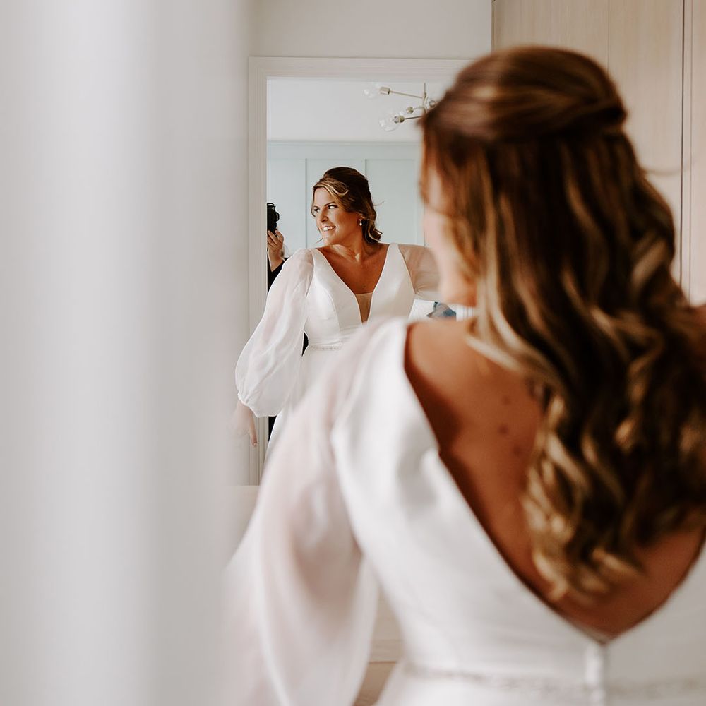 Bride wears sheer full sleeved wedding dress and her hair in loose curls 