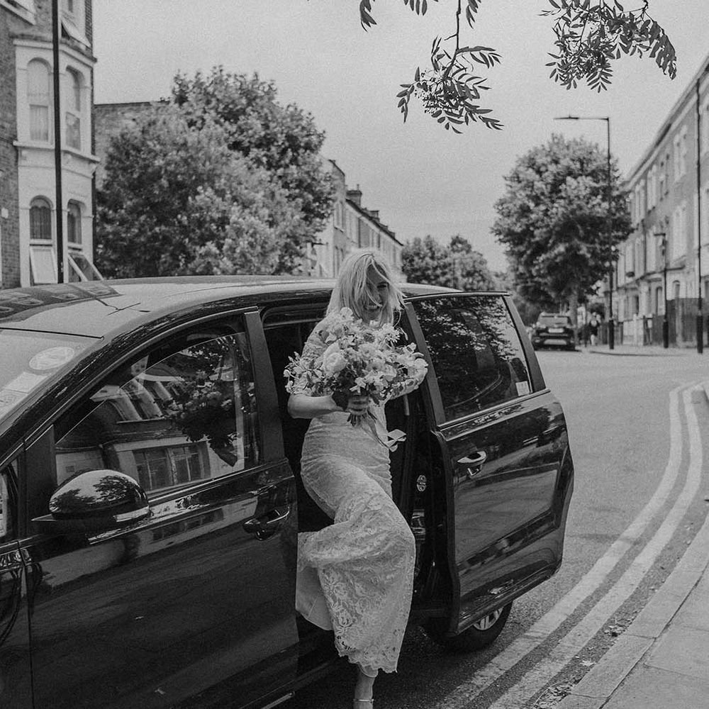 Bride in lace boho two piece and bright mixed floral wedding bouquet stepping out of car to Hackney Studios