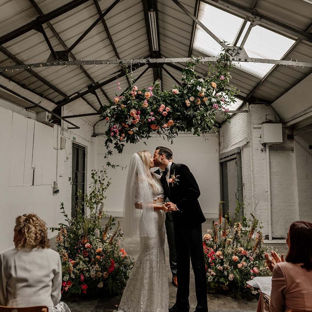 Bride in lace boho two piece and groom in black tux with bow tie and boutonniere sharing kiss at Hackney Studios