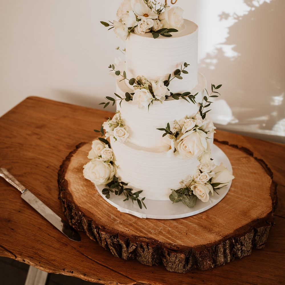 Three tier white frosted wedding cake with greenery decorations and a personalised cake topper 