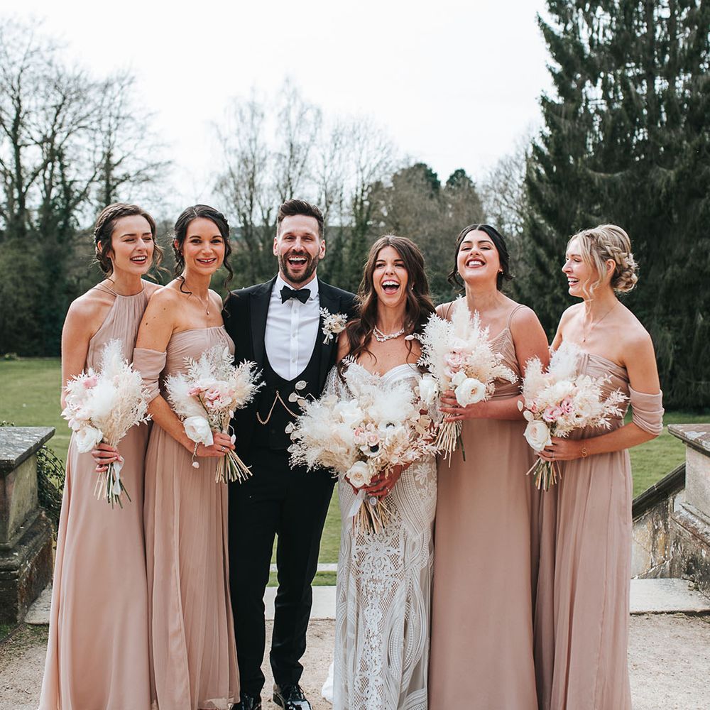 Neutral pink bridesmaid dresses in different styles laughing with the bride and groom for their country wedding at Hampton Manor 