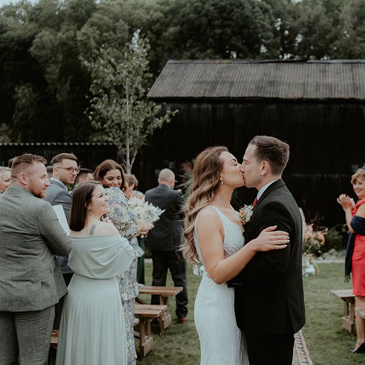 The bride and groom share a kiss at the end of the aisle as their guests applaud after the outdoor humanist wedding ceremony 