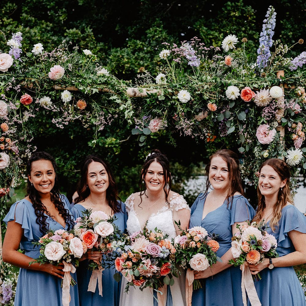 The bridal party photo with the bridesmaid in matching blue bridesmaid dresses and the bride in a Suzanne Neville wedding dress with spring bouquets 