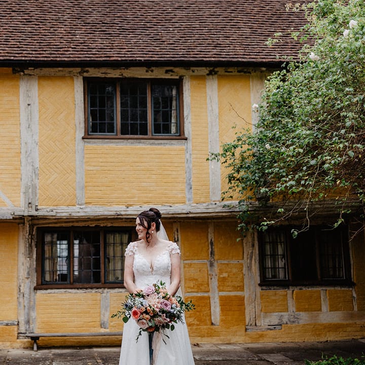 The bride in a flower wedding dress with the groom in front of rustic yellow building for cute couple portraits 