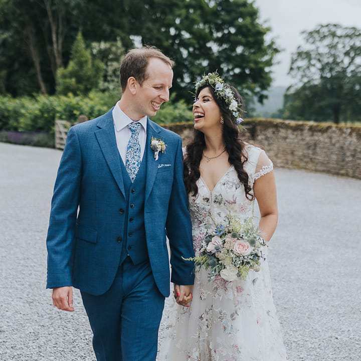 Indian British bride in a floral wedding dress and groom in a blue suit with floral tie at pastel wedding 