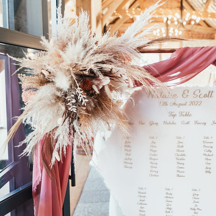 Hexagonal white and rose gold seating plan on copper frame decorated with pampas grass 