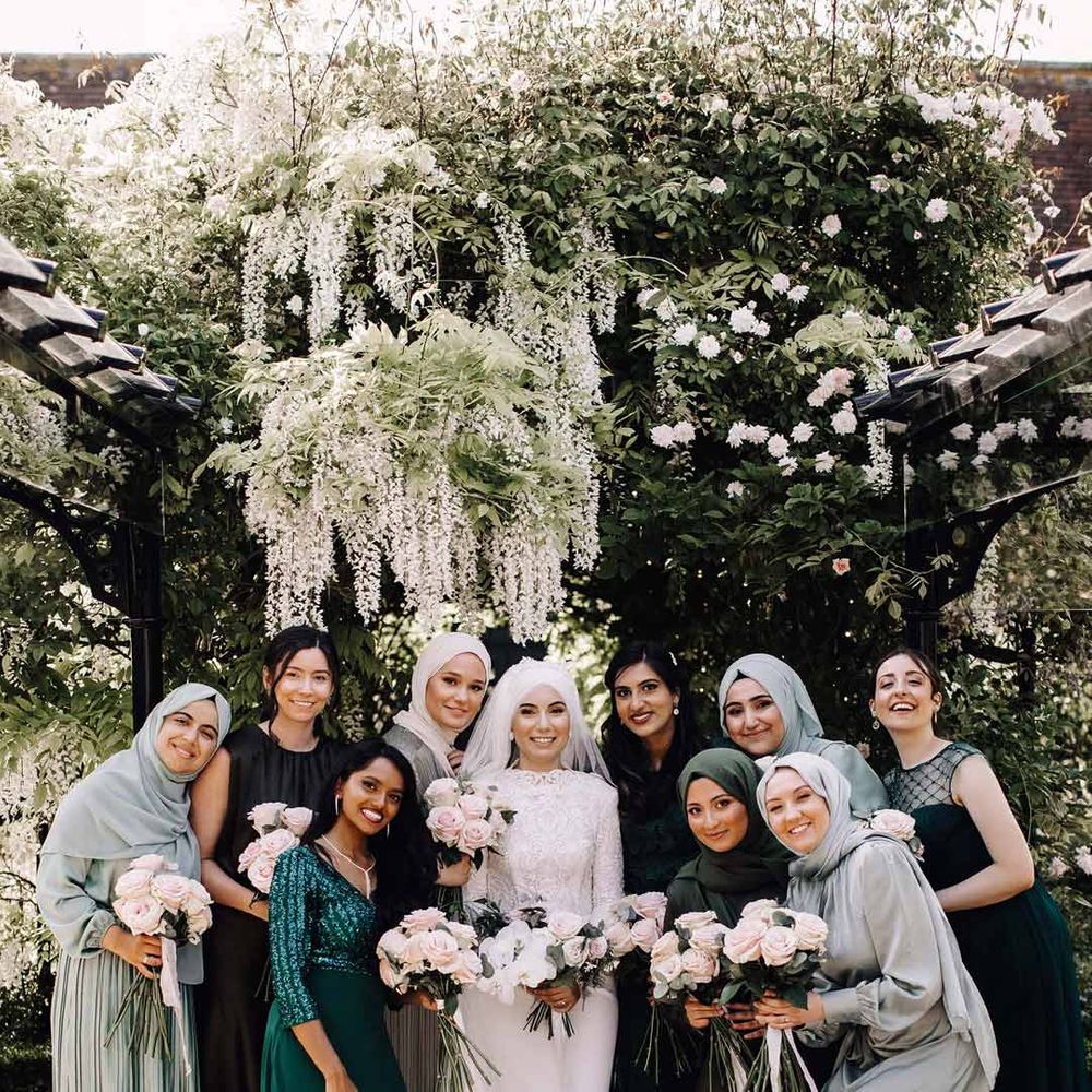 Bride in long sleeve wedding dress standing with bridal party in mismatched green bridesmaid dresses 