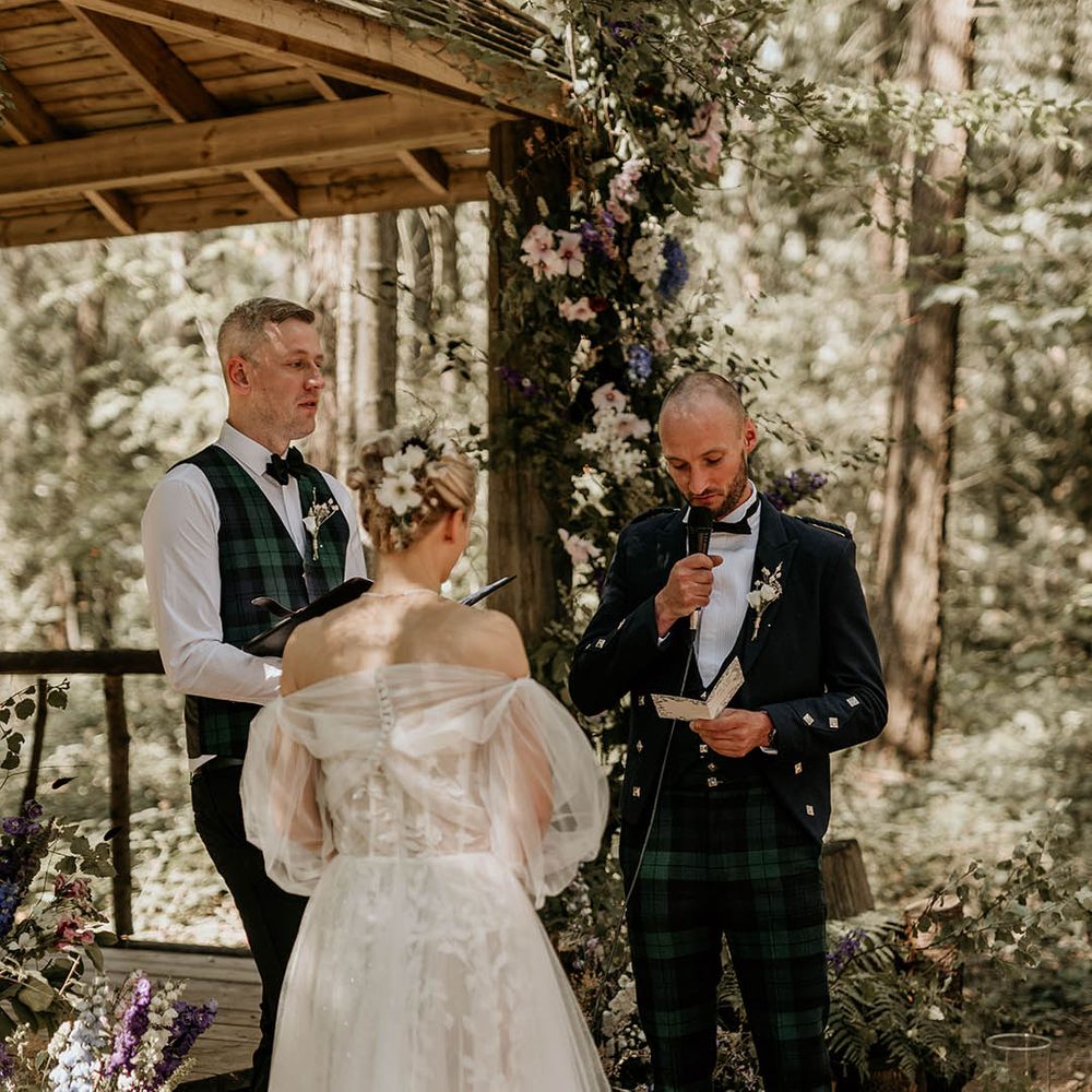 Bride in a Milla Nova wedding dress with detachable sleeves with groom wearing green checkered trousers reading out his wedding vows 