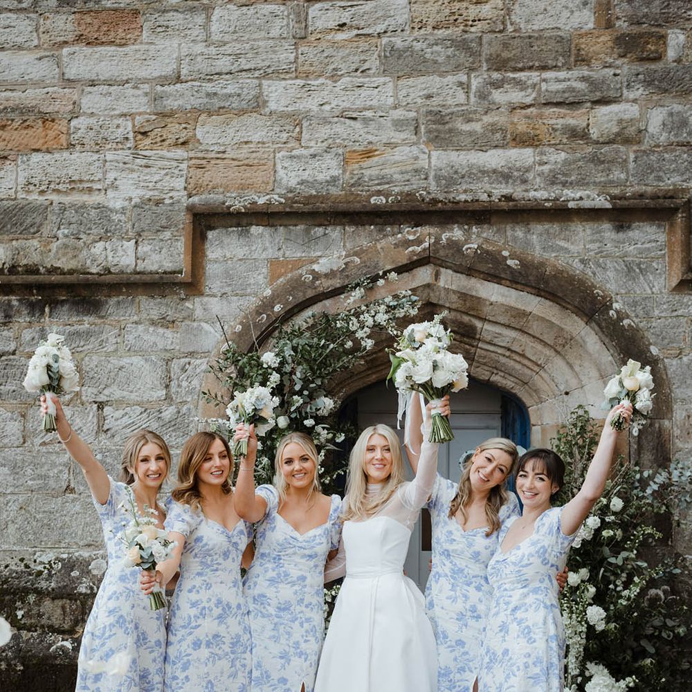 Bridal party in light blue and white floral patterned bridesmaid dresses at coastal wedding 