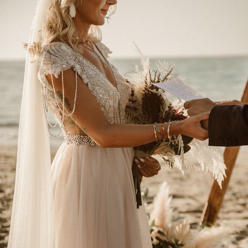 Bride and groom holding hands during boho beach wedding ceremony