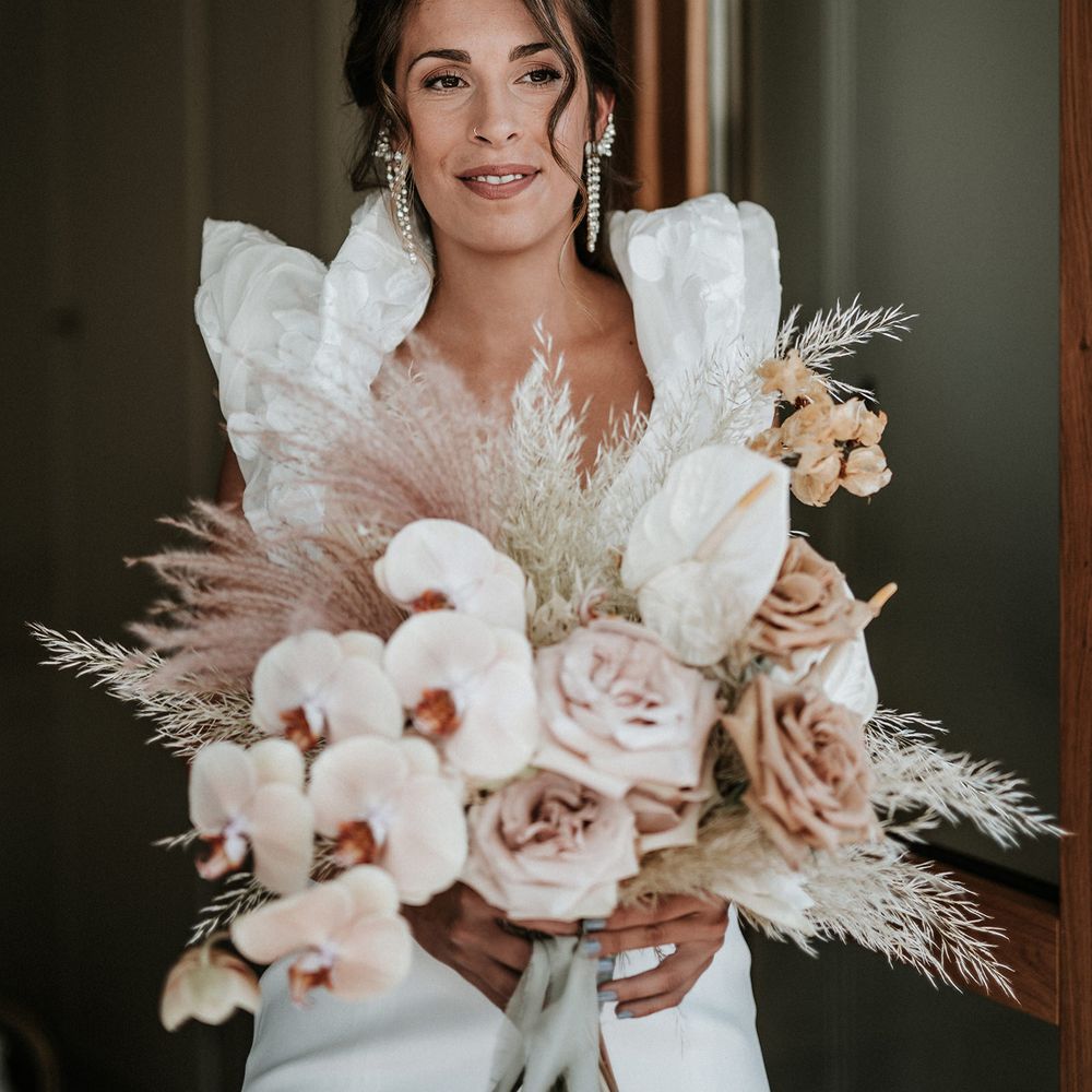 Destination bride holding a dusky pink and peach wedding bouquet with orchids, roses, anthuriums, and pampas grass. 