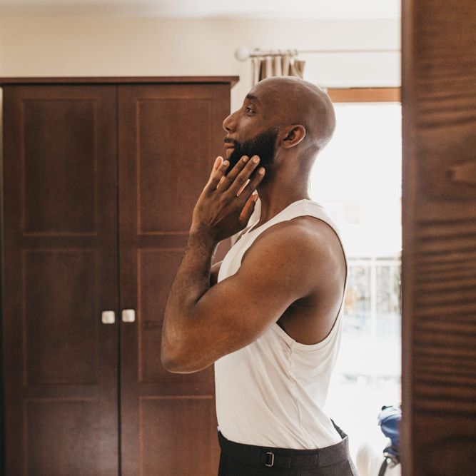 Black bearded groom in a white vest getting ready on the wedding morning 