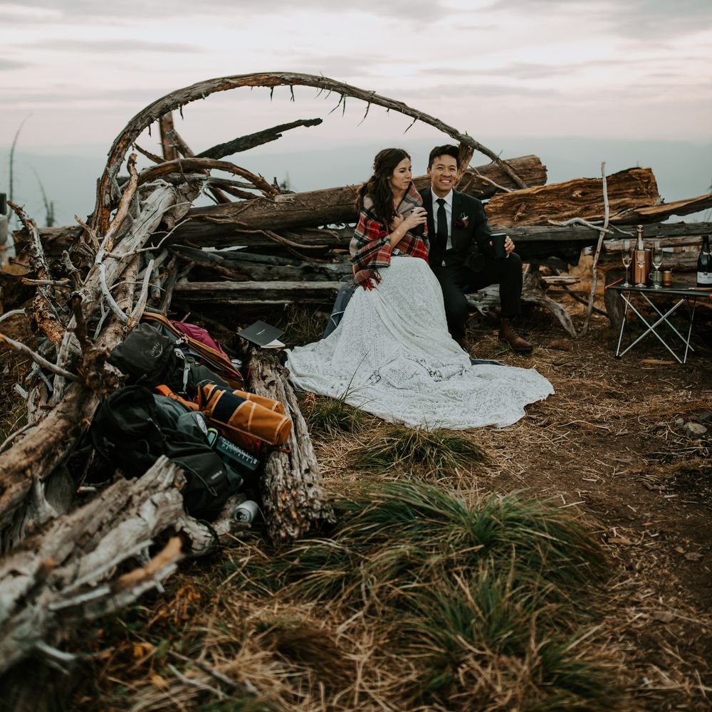 Bride & groom sit with one another in rustic setting on mountain
