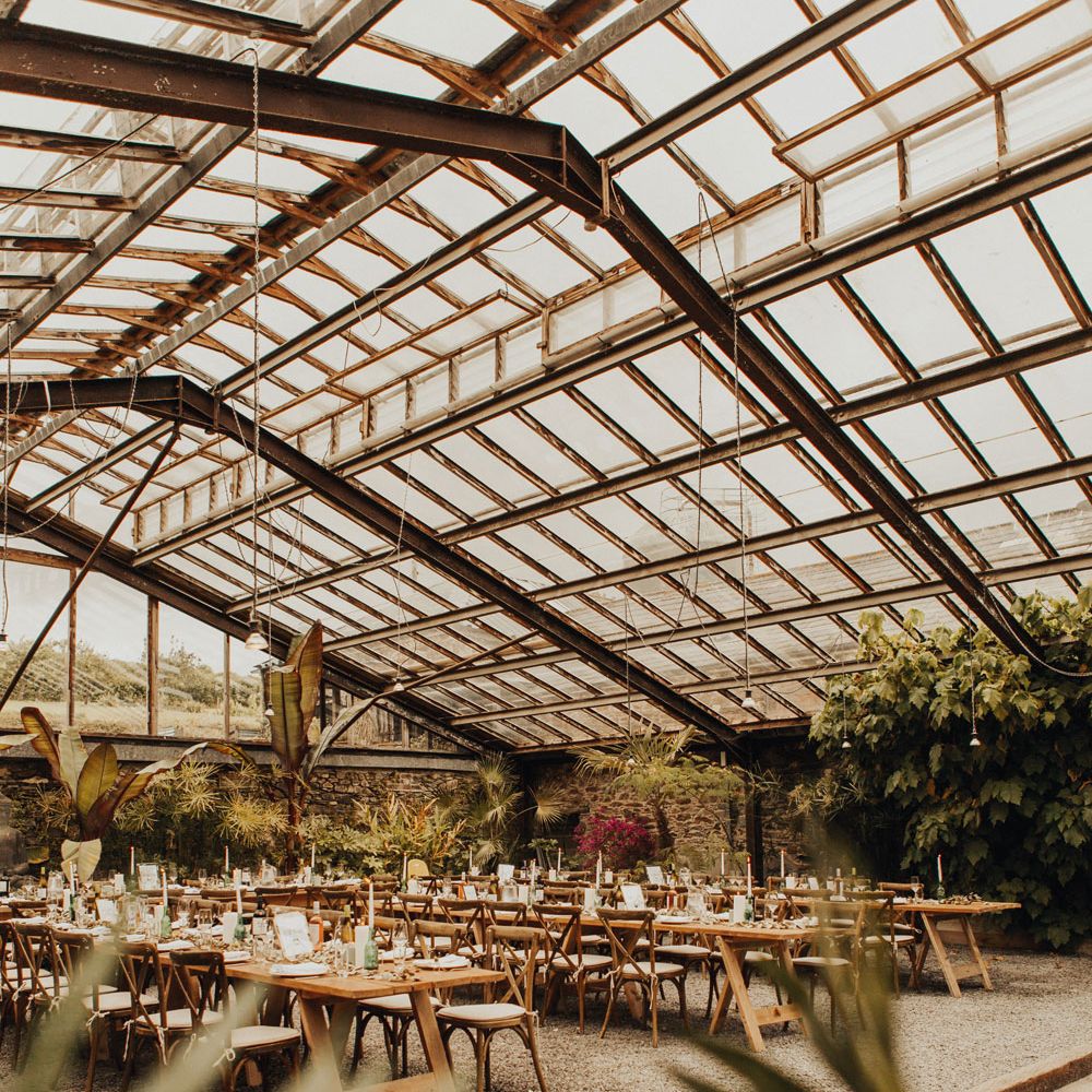 Interior of the glasshouse at Anran Devon set up for a wedding reception with long wooden tables, wooden chairs and candles 