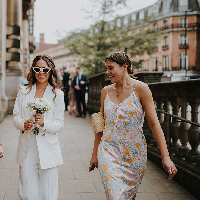 Bride in a Reiss suit and sunglasses holding a white flower bouquet 