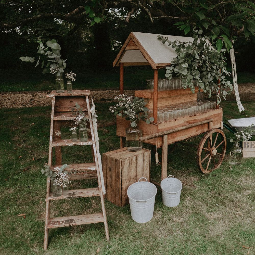 Outdoor bar cart with glasses, beer barrow and wooden boxes with milk churns at Isle of Wight wedding with macrame wedding decor