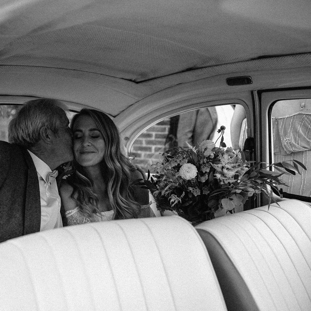 Bride in Grace Loves Lace bardot wedding dress holding mixed bridal bouquet sits in the back of VW bug with man in suit before Isle of Wight wedding