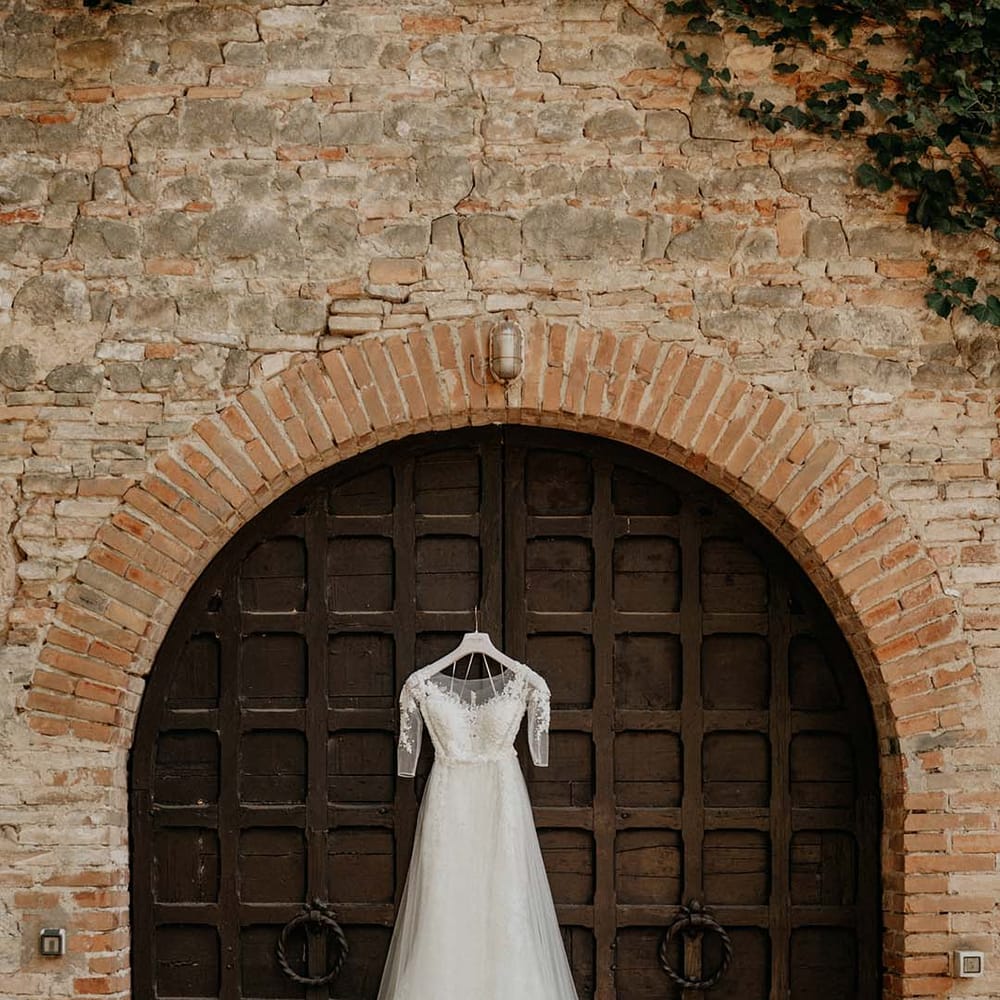 Brides dress hangs up against medieval style door next to brickwork  | Royal Studio
