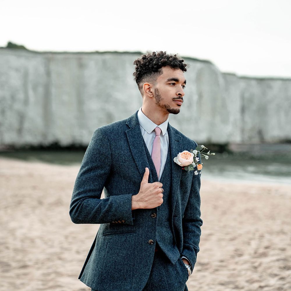 Stylish groom in a three-piece blue wool suit and light pink satin tie 