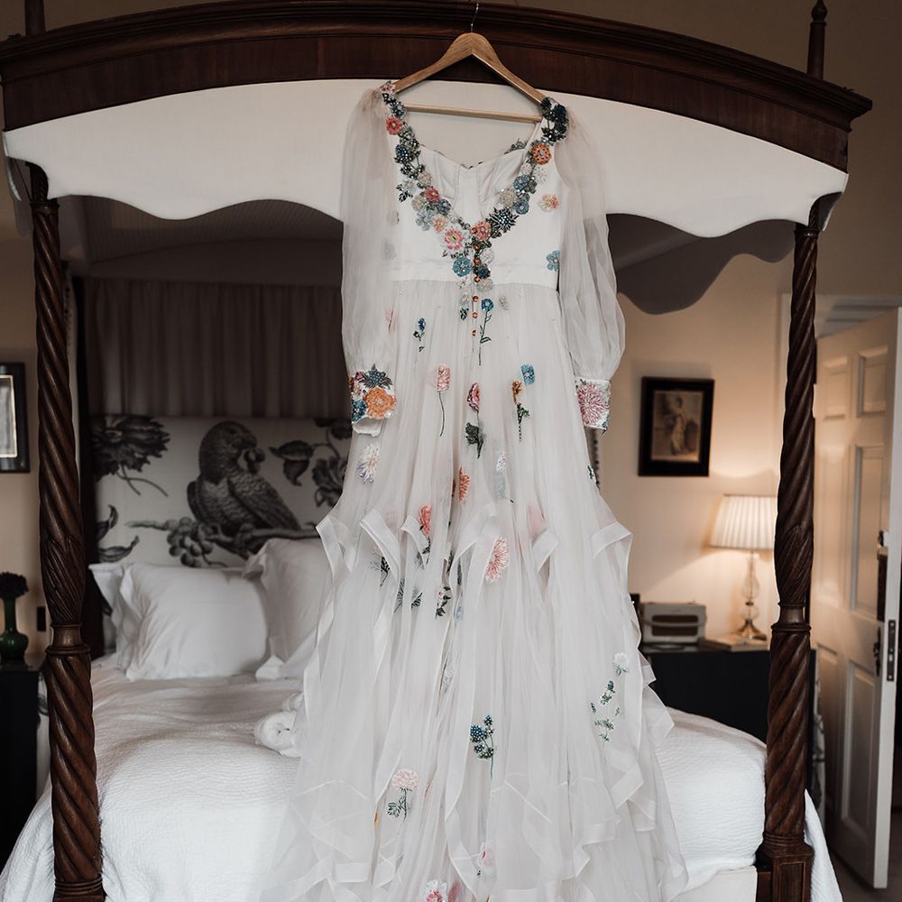 Mesh sleeve embroidered Victoria Sanders wedding dress with floral embroidery hangs from bed
