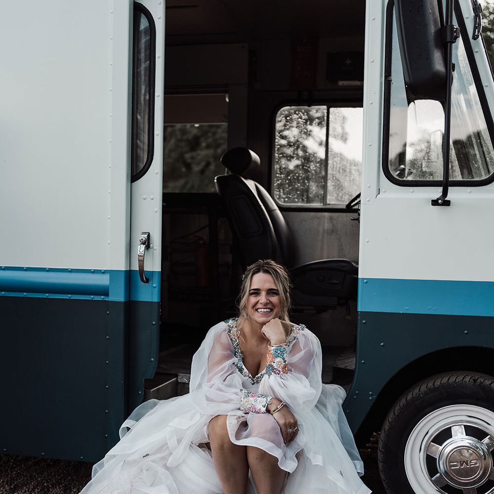 Smiling bride in bespoke Victoria Sanders wedding dress and white Nike Air Max trainers sits in van at Iscoyd Park