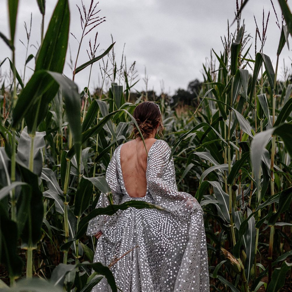 Bride in a silver sequin wedding dress walking through some crops at her home stretch tent wedding 