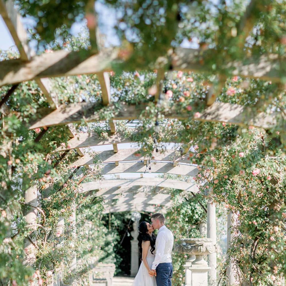 Bride & groom kiss underneath pergola on their wedding day