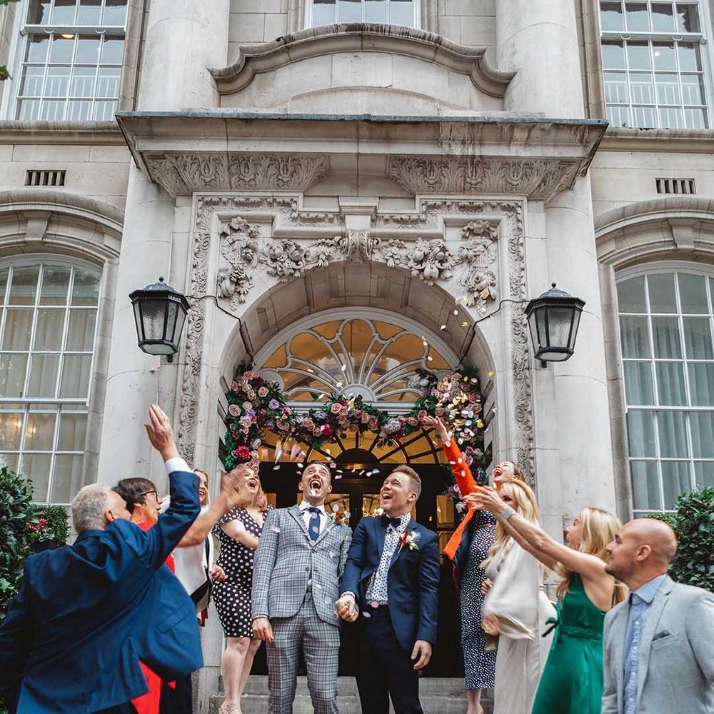 Grooms stand on Chelsea Old Town Hall steps outdoors as confetti is thrown around them