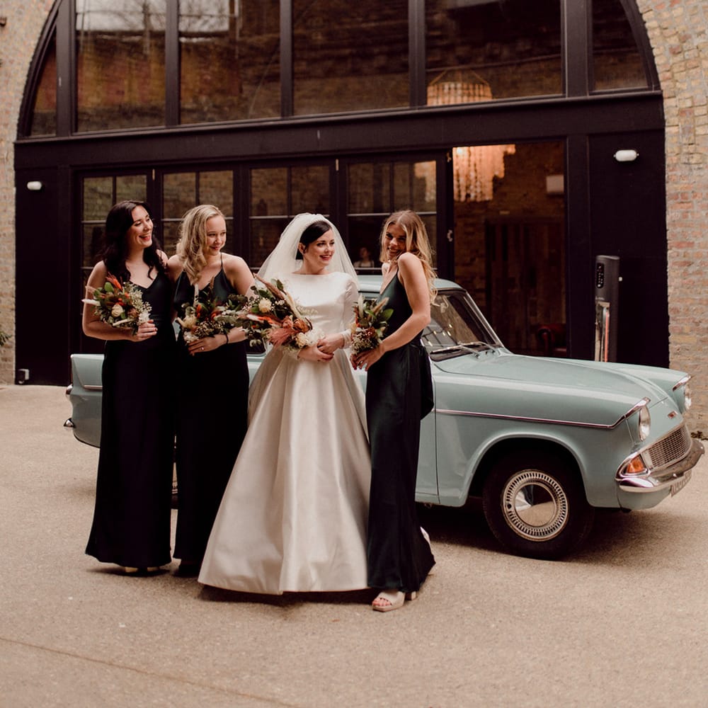 Wedding party pose in front of baby blue vintage car with dried flower wedding bouquets for LGBTQI+ wedding