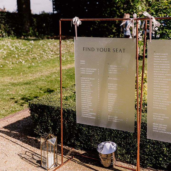 Frosted seating chart and table plan on copper frame decorated with white ribbons and candles in geometric lanterns 