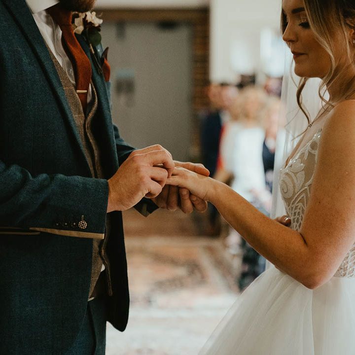 Groom in blue suit and brown waistcoat puts the ring on the bride's finger during their wedding ceremony 