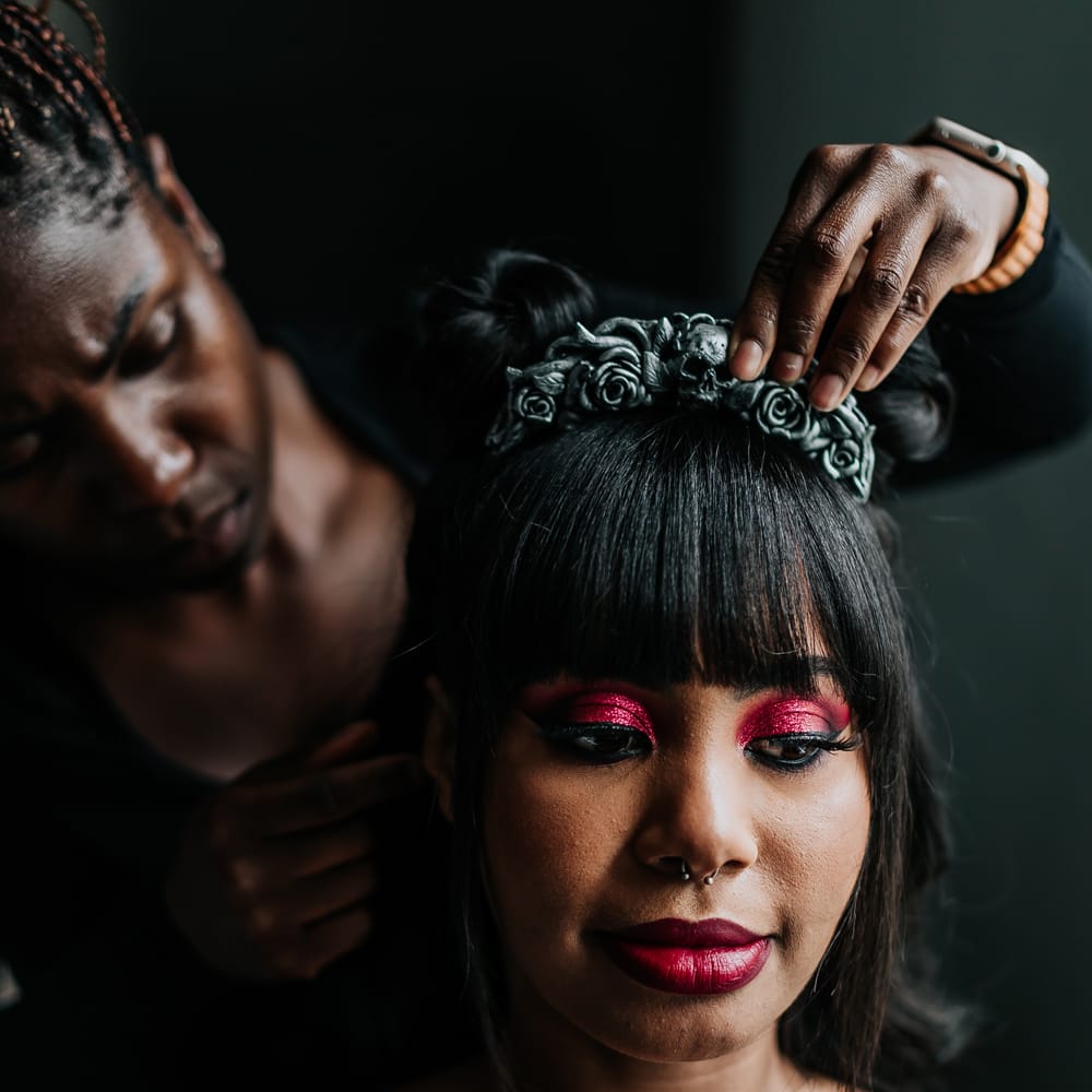 Black bride wears bold pink glitter eyeshadow and red lipstick as skull crown is placed in her hair 