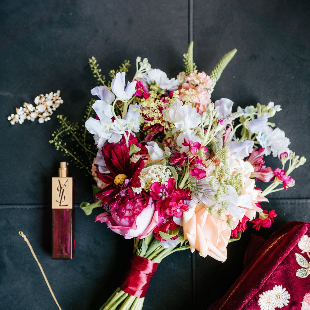 Bright floral bridal bouquet tied with bright pink ribbon beside YSL bridal perfume 