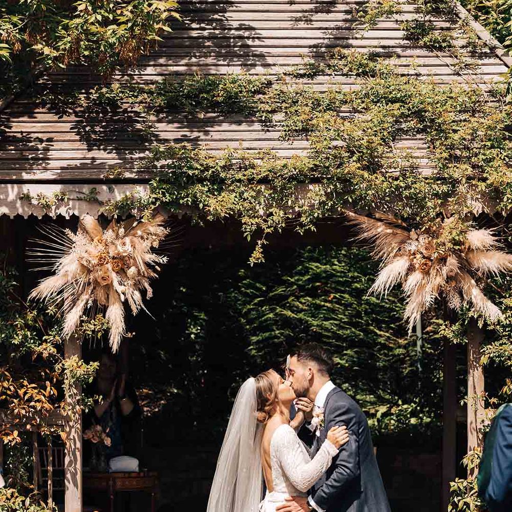 Bride in scoop back long sleeve wedding dress and groom in dark tux embracing at Pennard House with pampas grass floral arrangements 