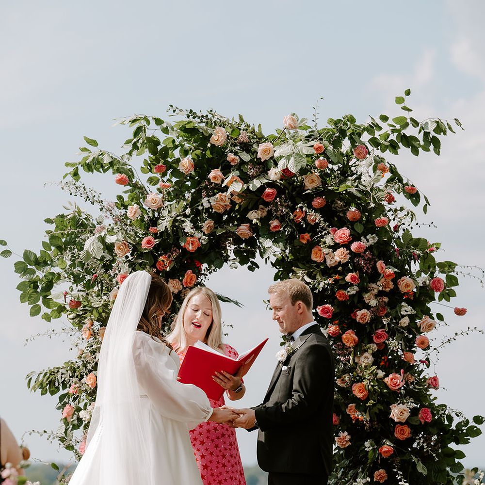 Bride & groom marry at Botley Hill Barn in front of floral archway 