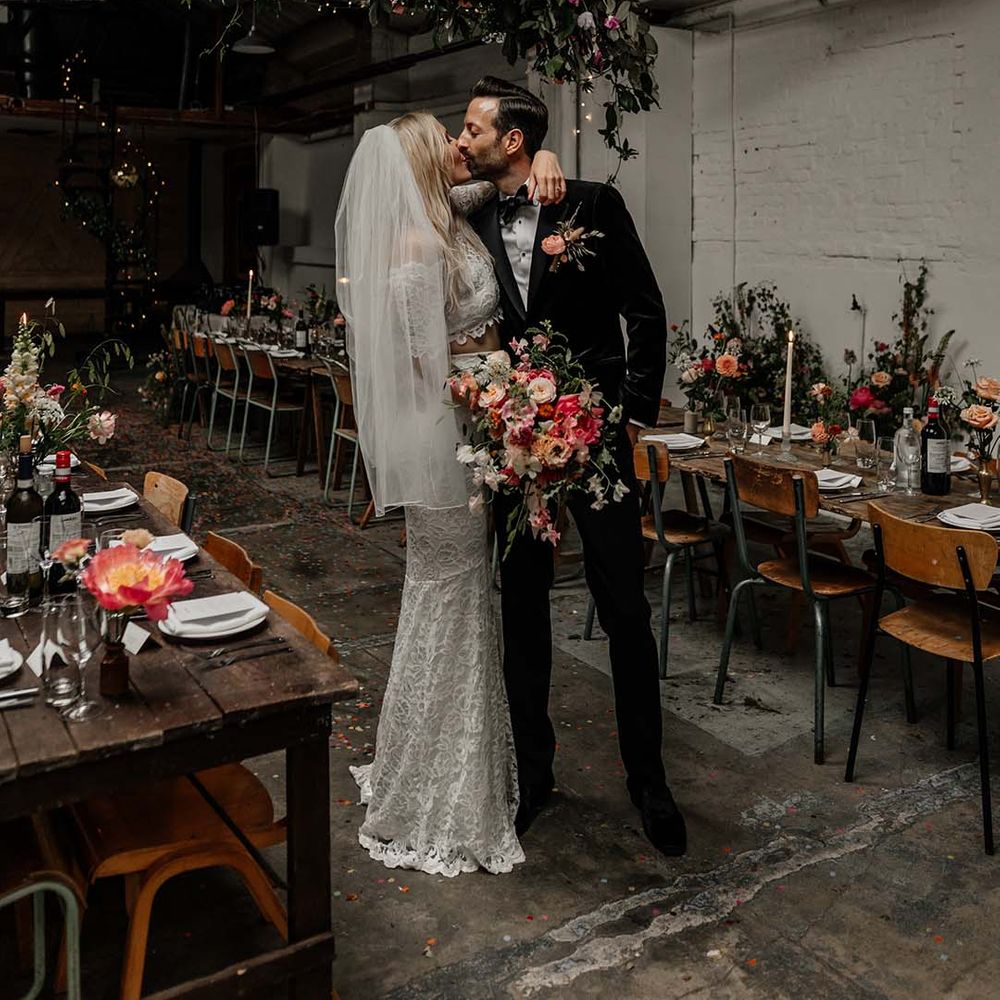 Bride and groom standing in Hackney Studios wedding reception with large hanging foliage decoration, fairy lights and neutral wedding tablescapes 