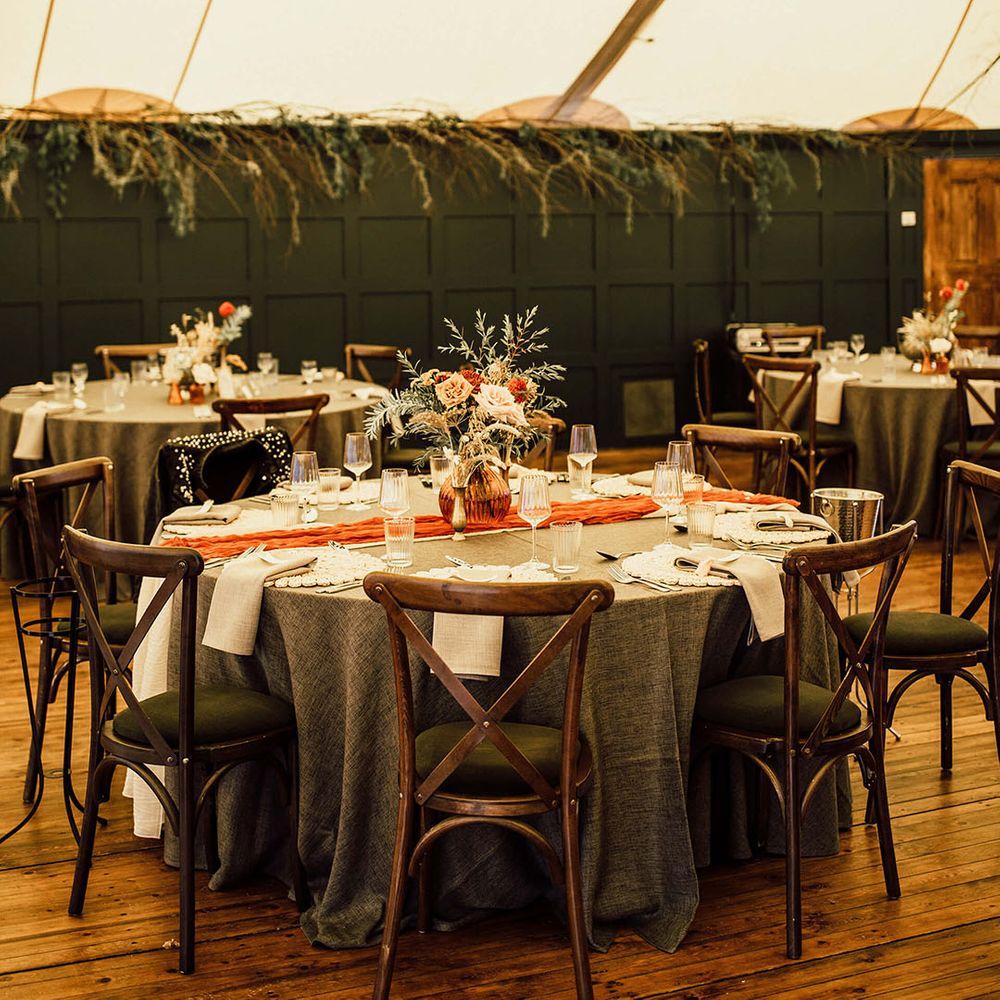 Hanging green foliage installation above round tables with green tablecloths and orange table runners 