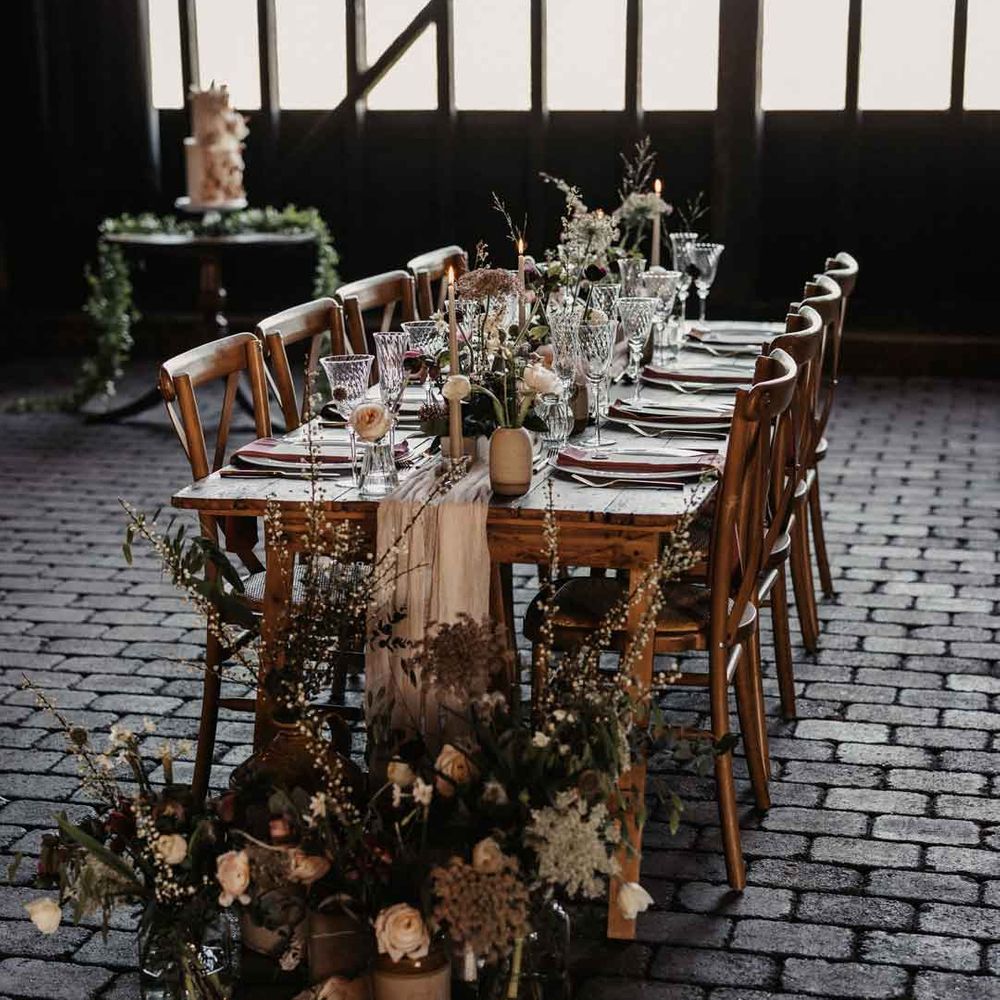 Rustic luxe wedding tablescape at Elmley Nature Reserve wedding venue with white cloth table runners, foliage, baby's breath, eucalyptus and dried flower floral arrangements, neutral tapered candles and small ceramic vases 