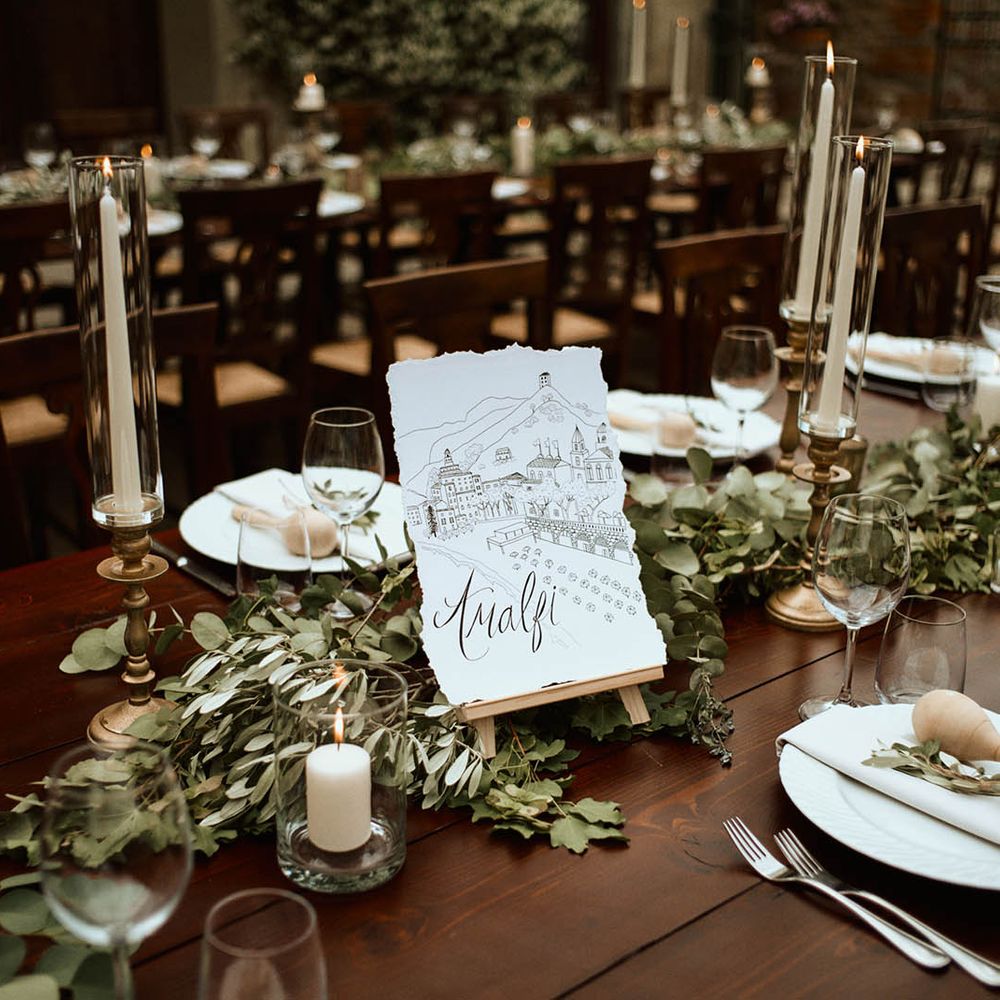 'Amalfi' table name with eucalyptus and tapered white candles at wedding breakfast