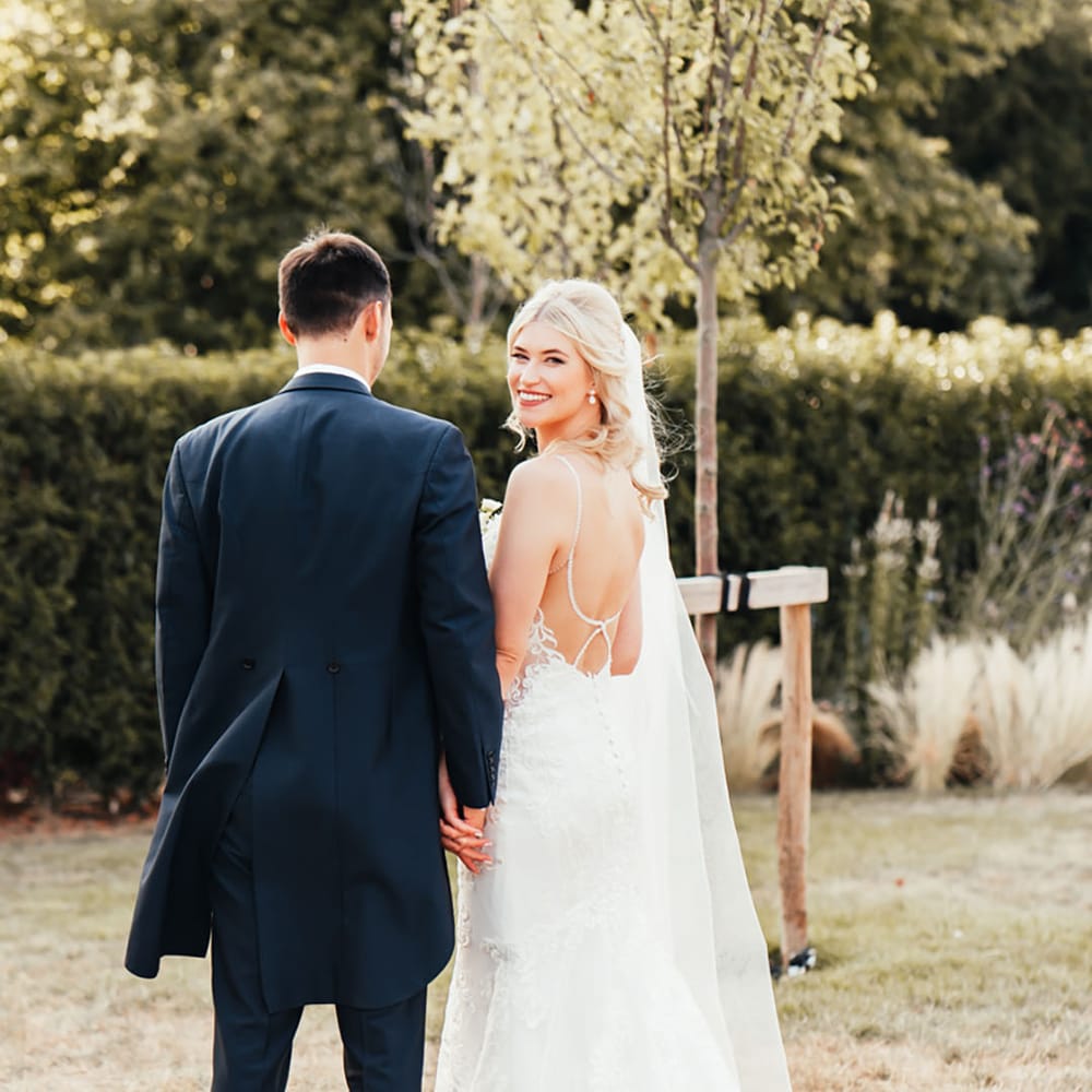 Bride in open back wedding with diamond embellished detail on her wedding dress with mermaid lace skirt walking with the groom 