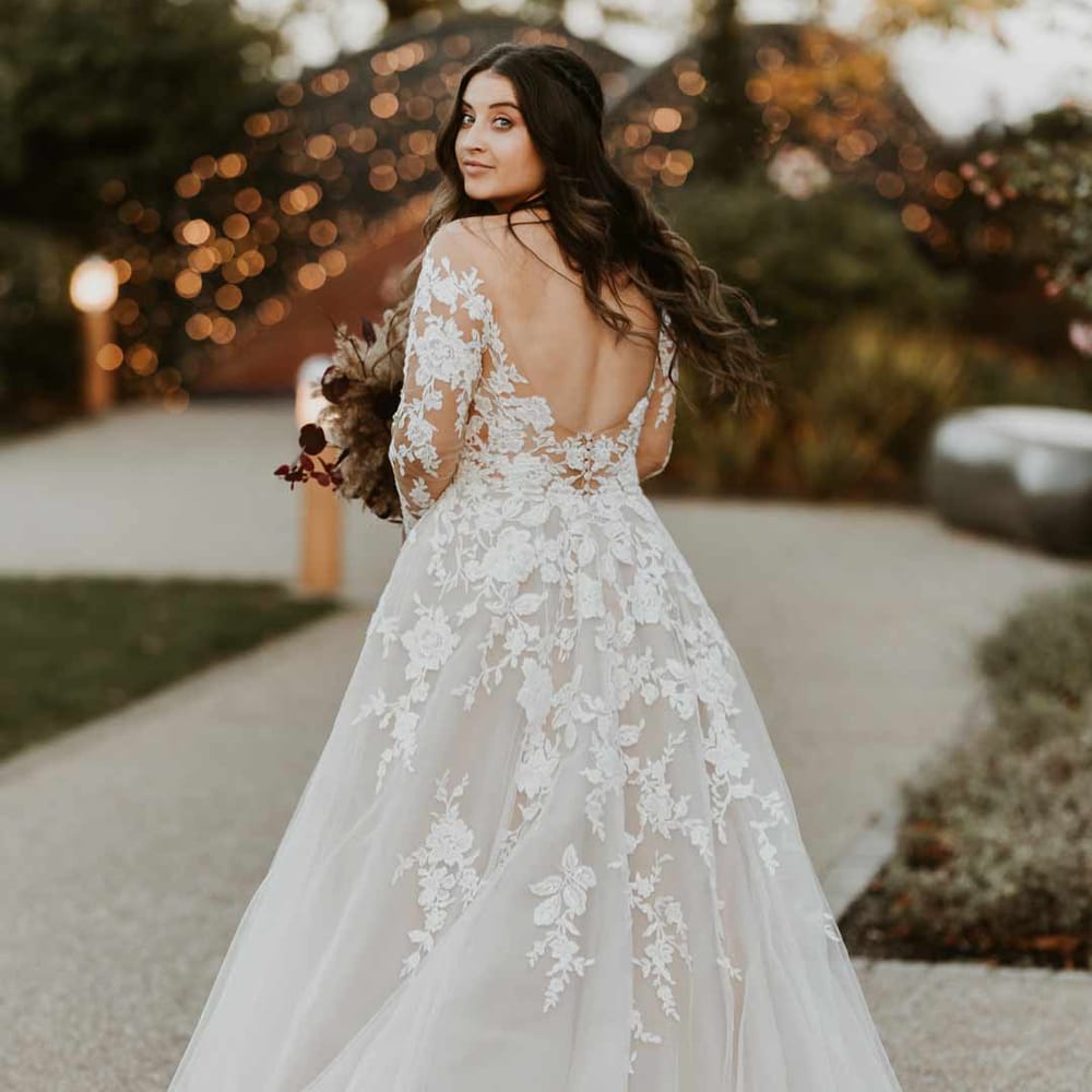 Bride wearing long sleeve lace illusion sleeve wedding dress with overlay holding large autumnal boho dried flower bouquet 