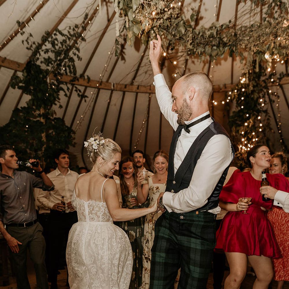 Bride in floral wedding dress with groom in green checkered trousers and black waistcoat having their first dance together 